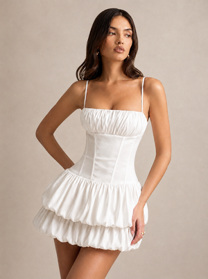 Three-quarter front view of the white corset mini dress with thin straps and a voluminous bubble skirt.
